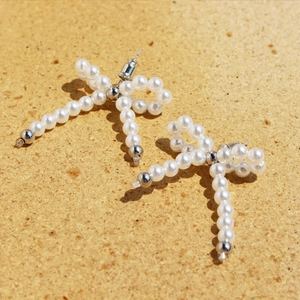 Elegant pearl bead bow earrings with silver accents on a natural cork background