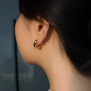 Detailed view of polished 18K gold C-shaped earrings worn to show modern metallic texture
