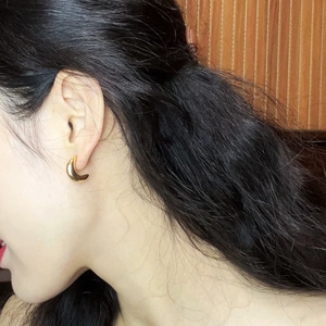 Detailed shot of a minimalist gold crescent C-shaped earring on a woman's earlobe