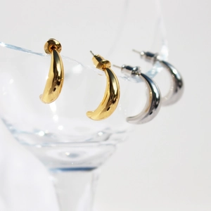 Polished gold and silver crescent C-shaped stud earrings on glass rim