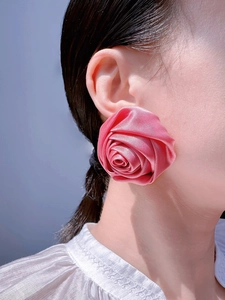 Dettaglio degli orecchini a rosa in raso rosa con petali 3D indossati su sfondo blu