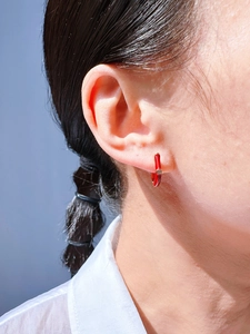Macro detail of red enamel hoop earring with a sparkling zircon on a model