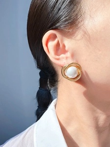 Close-up of elegant gold spiral stud earrings with a large white pearl center on model