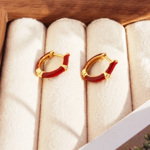 Elegant gold earrings with burgundy enamel and zircon inlay on a beige velvet display