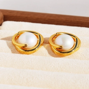 Elegant gold hollow layered earrings with white pearls on a soft jewelry display tray