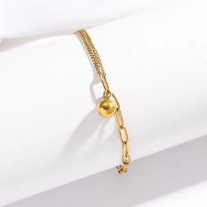 Detailed view of a gold paperclip chain bracelet with a polished metal bead pendant