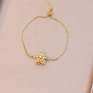 Detailed view of rotating five-petal flower charm with inlaid zircons on gold bracelet