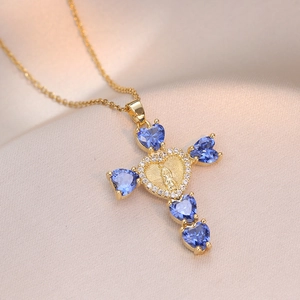Gold cross necklace with blue heart stones and Virgin Mary engraving on silk background