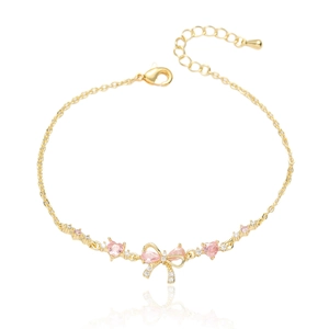 Détail du bracelet doré avec cœurs roses, nœud élégant et zircons brillants sur fond blanc