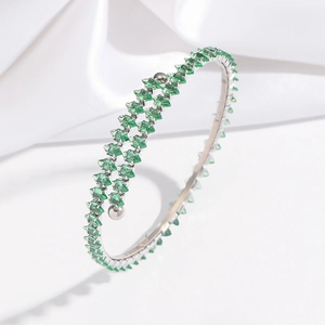 Détail du bracelet argenté avec cristaux verts carrés posé sur un tissu en soie blanche