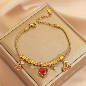 Elegant gold titanium steel bracelet with red heart and cherry charms on a jewelry box