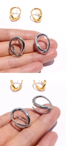 Detailed view of intertwined geometric gold and silver hoop earrings held by hand