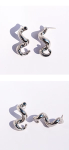 Détails macro de boucles d'oreilles spirales en métal liquide argenté ondulé
