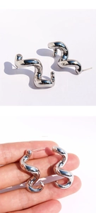 Détail macro de boucles d'oreilles vagues argentées avec texture métal liquide poli
