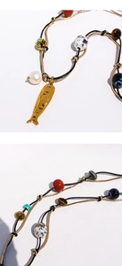 Dettaglio della collana con pendente a pesce dorato, perle e pietre occhio di tigre