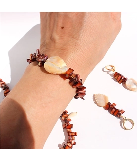 Detailed shot of handmade shell leaf charms and red beaded bracelets with gold earrings