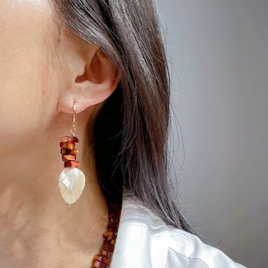 Detail of leaf shell earrings with reddish-brown beads worn by a model in a white shirt