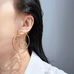 Gros plan de boucles d'oreilles dorées à triple cercles entrelacés portées par modèle