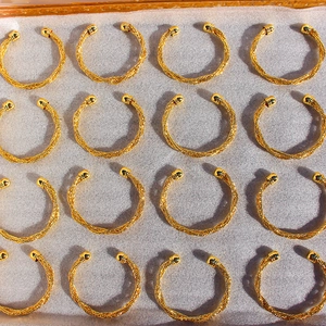 Dettaglio macro di bracciali rigidi aperti in metallo intrecciato dorato in un vassoio