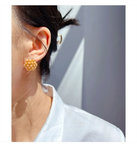Close-up of orange floral puff earrings with white pearls on a model's ear