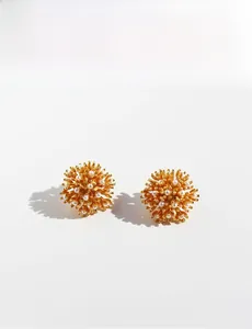 Detailed close-up of golden sunburst floral earrings with pearls on white background