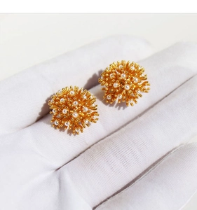 Macro shot of gold floral pearl stud earrings displayed on hand for size perspective