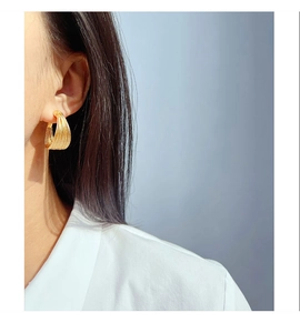 Detailed view of layered gold C-shaped hoop earrings worn by a model in soft light