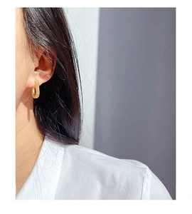 Close-up of golden U-shaped earrings with textured weave and rectangle gemstone inlay