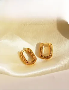 Detailed close-up of golden U-shaped hoop earrings with textured metal granulation