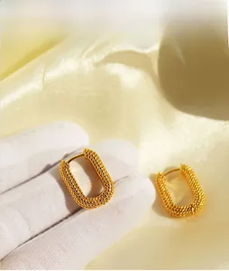 Macro shot of gold U-shaped earrings with intricate beaded texture on yellow silk