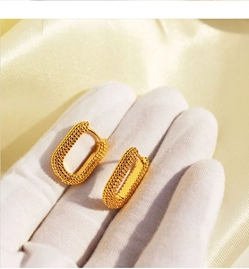 Detail of gold rectangular earrings with beaded texture held against silk background