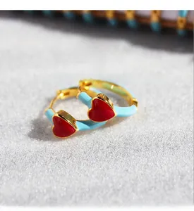 Detail of blue enamel hoop earring in gold plated brass with red zircon heart