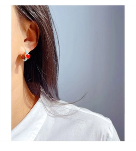 Close-up of red heart pendant with light blue enamel hoop earring on model