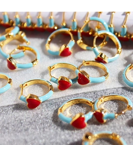 Macro shot of blue enamel hoop earrings with red heart pendants in a stacked display