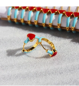 Detail shot of light blue enamel hoop earrings with red heart patterns and gold finish