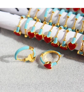 Macro detail of sky blue enamel hoop earrings with red heart charms on white display