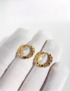 Detail of bamboo joint style gold earrings with paved white zircons on a white background