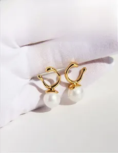 Detail showing irregular gold streamline rings with round pearls on a white surface