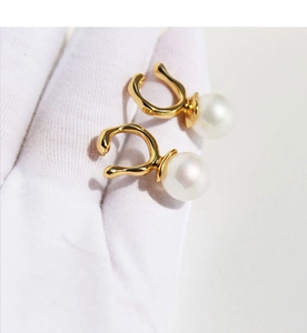 Detail of gold geometric ear cuffs with round white pearls held by a gloved hand