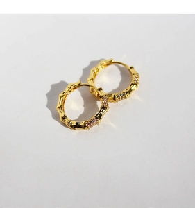 Macro detail of gold bamboo-style hoop earrings with cubic zirconia inlay texture