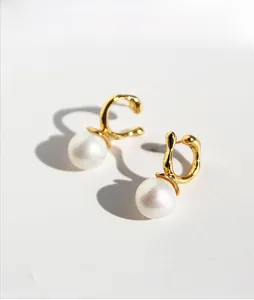 Detail showing irregular gold metal hooks with large round white pearls in a modern style