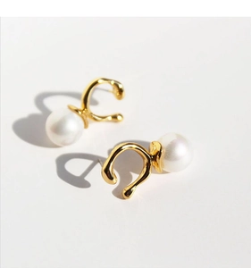 Close-up of gold irregular U-shape earrings featuring glossy white faux Mabe pearls