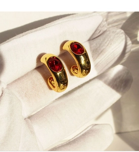 Vue macro des boucles d'oreilles C dorées avec zircone ovale rouge incrustée