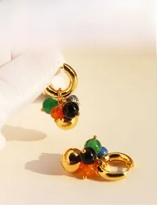 Detailed close-up of colorful emerald, orange, and black beads on gold hoop earrings