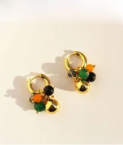 Detail of drop earrings with gold beads and multi-colored agate stones on off-white surface