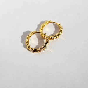 Minimalist gold bamboo hoop earrings with sparkling cubic zirconia on a gray background