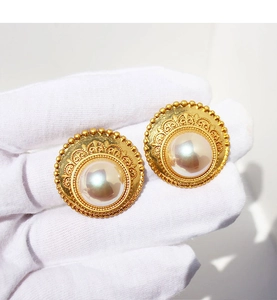 Dettaglio di orecchini vintage in pizzo dorato con grandi perle su guanto bianco