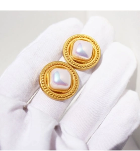 Dettaglio degli orecchini vintage dorati con perle quadrate iridescenti e bordi in pizzo