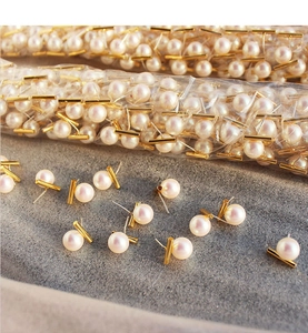 Macro detail of round pearl earrings with minimalist gold metal bar and silver pins