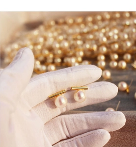 Detail of round pearl earrings with gold bar studs held by a gloved hand